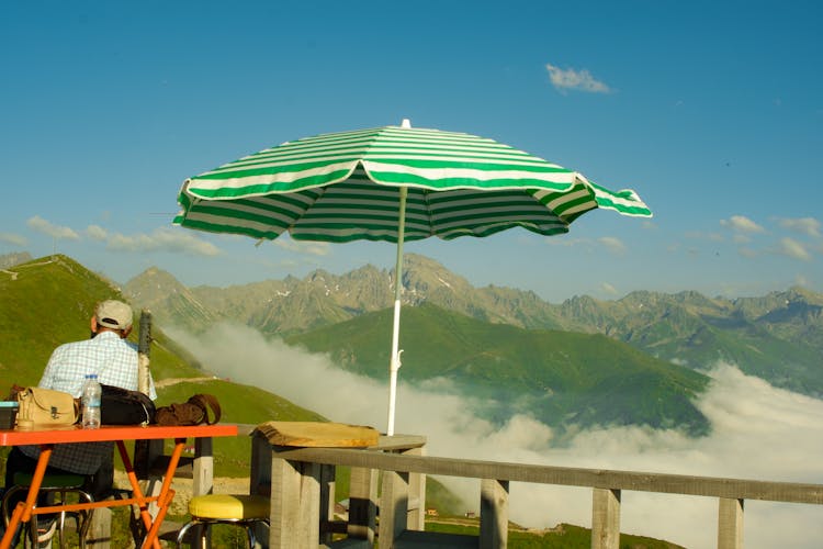 Man Sitting With Umbrella In Mountains