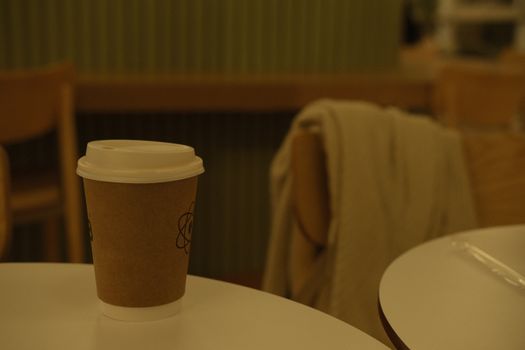 Warm indoor setting featuring a paper coffee cup on a table in a cozy cafe environment.