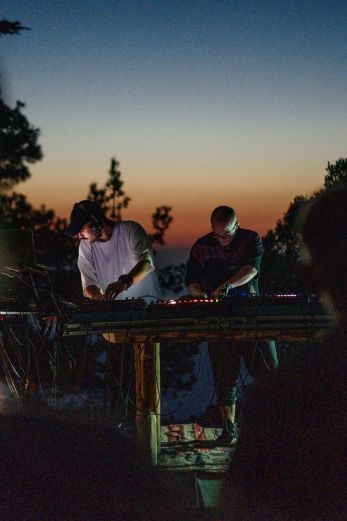 Free Two DJs perform outdoors with electronic music as the sun sets in the background, creating a vibrant party atmosphere. Stock Photo