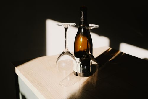 Free Artistic still life of wine bottle and glasses casting shadows in sunlit room. Stock Photo