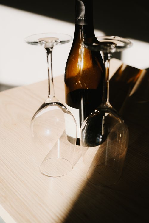Free Sunlight casts artistic shadows on a wine bottle and glasses on a wooden table. Stock Photo