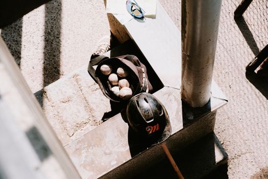 A sunlit scene with a baseball bag, balls, and helmet on urban stairs, perfect for sports imagery.