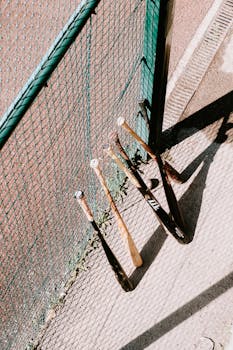 High-angle view of baseball bats leaning against a fence on a sunny day.