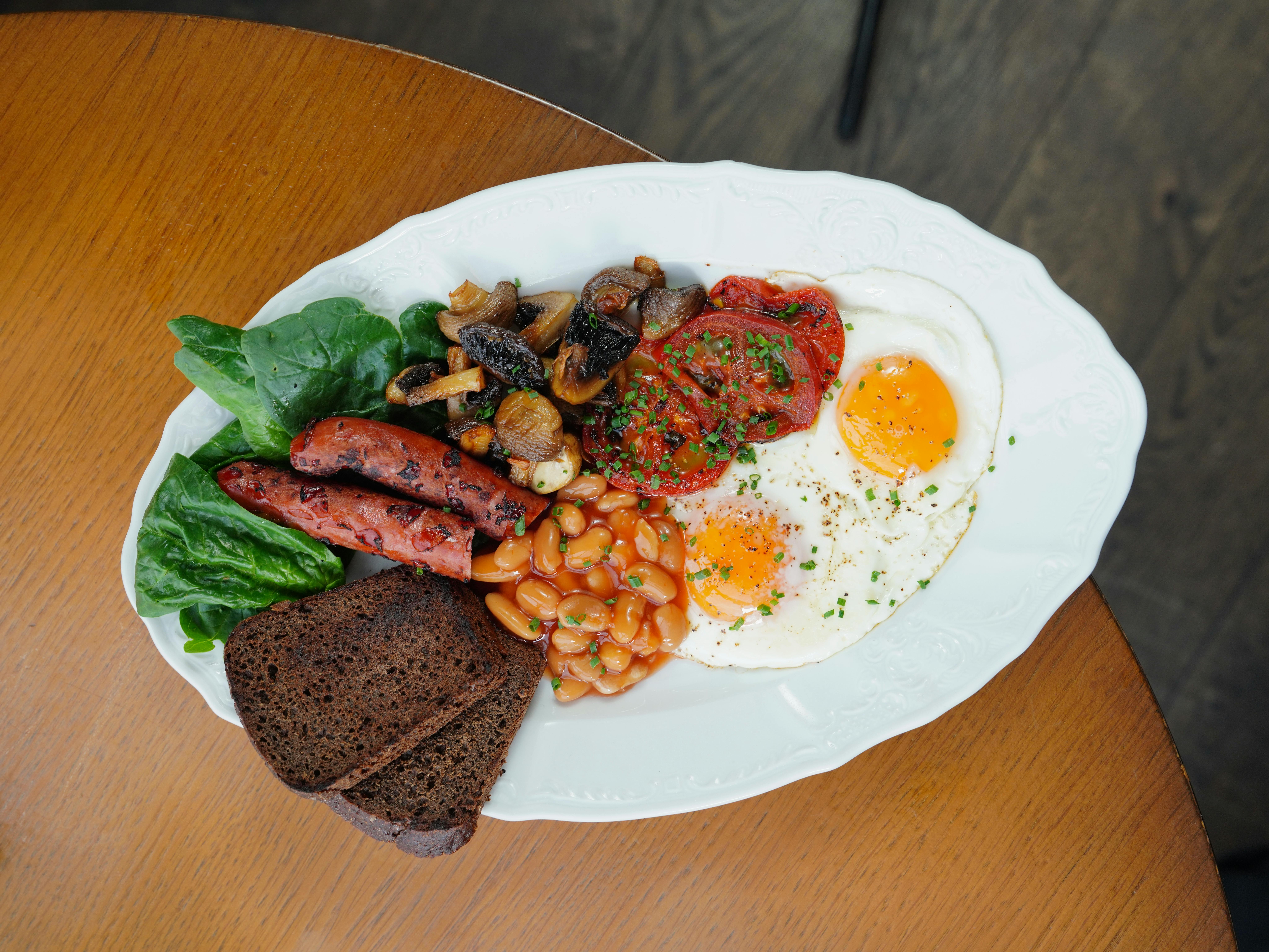 Tasty full English breakfast with eggs, beans, sausage, and toast on a plate.