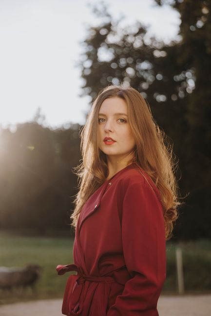 Fashionable redhead woman in a red coat posing outdoors in Berlin park during sunset.