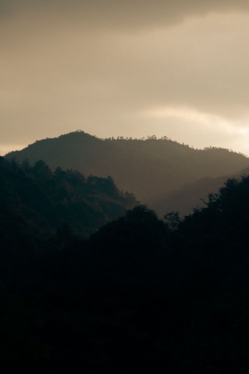 Free Serene view of rolling hills and forested mountains during sunset. Stock Photo