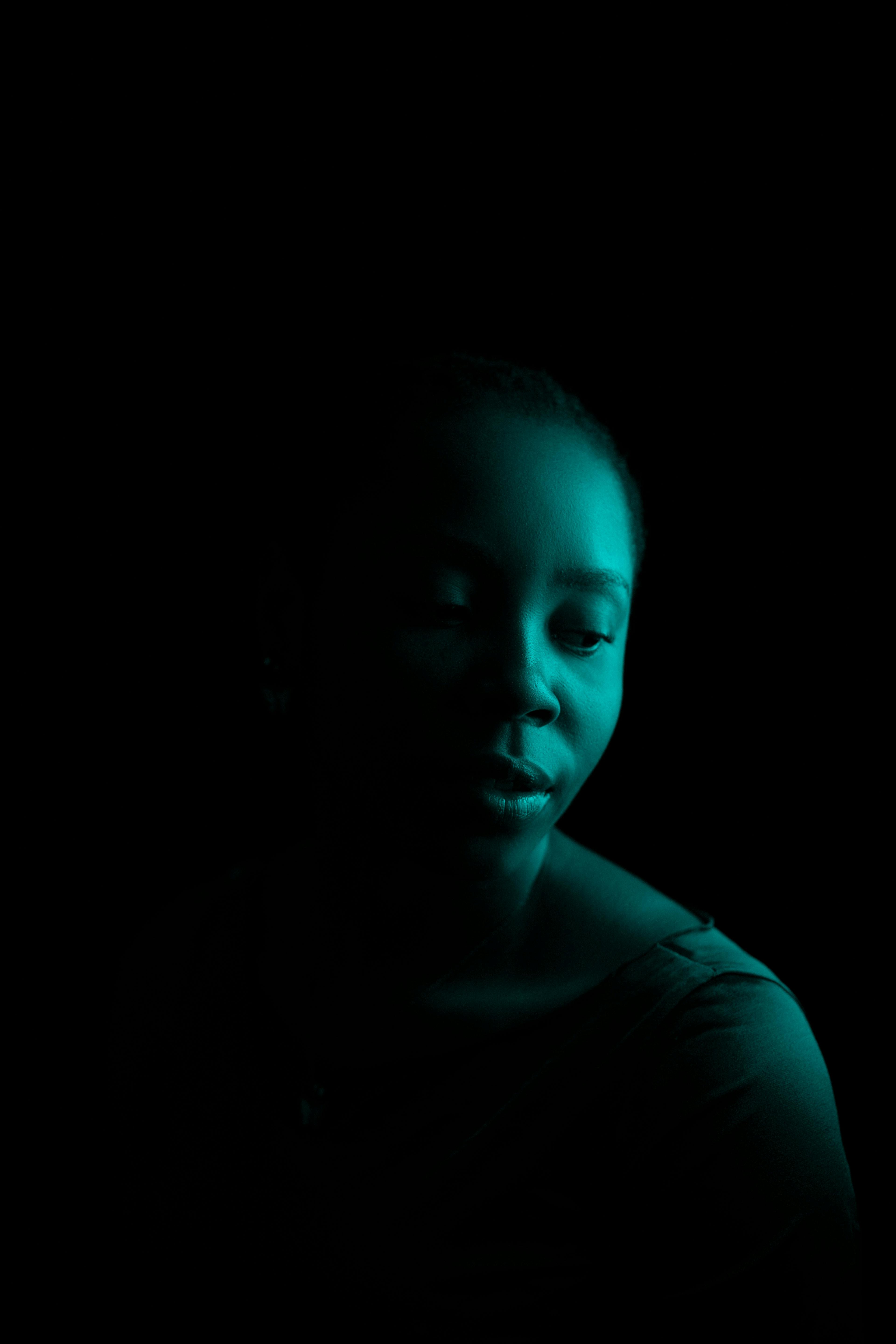 Artistic portrait of an African woman in blue spotlight with a shadowed background.