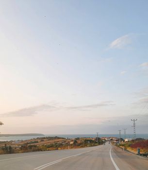 A peaceful rural road leading to a coastal village during a stunning sunset.