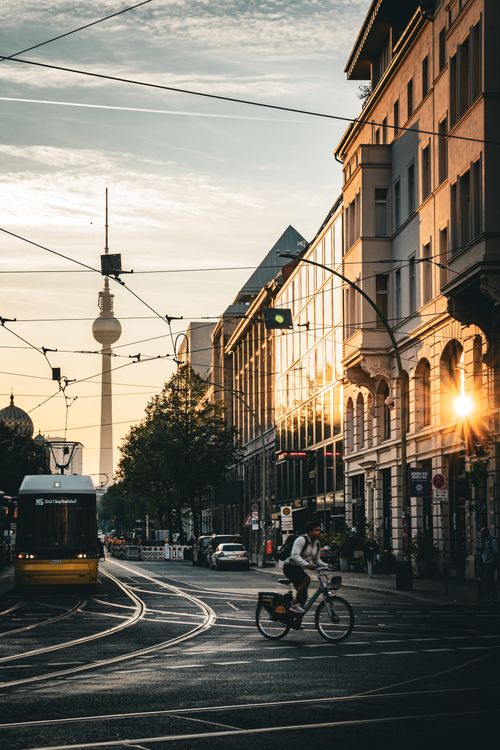 Free Dynamic Berlin street scene featuring cyclist, tram, and Fernsehturm at dusk. Stock Photo
