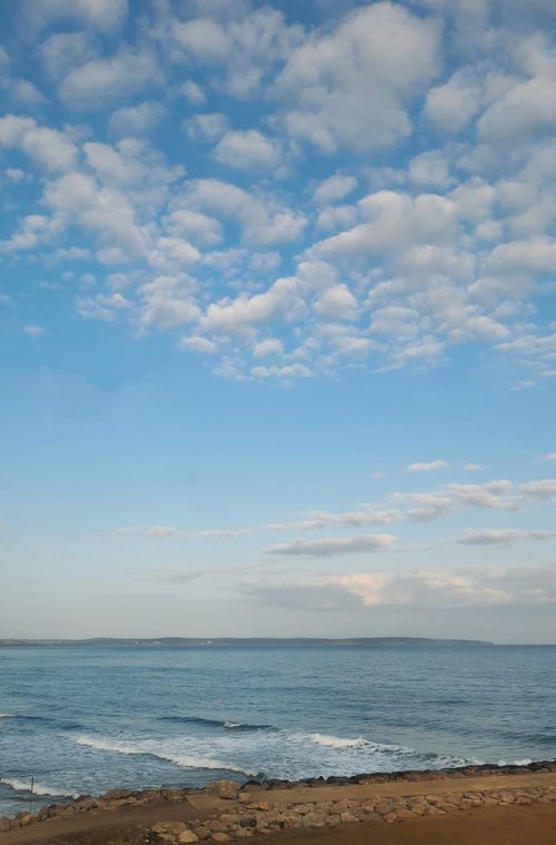 Free Serene beach scene with clear blue sky and scattered clouds, perfect for relaxation. Stock Photo