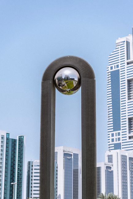 A striking modern sculpture set against the iconic Dubai skyline, showcasing urban architecture.