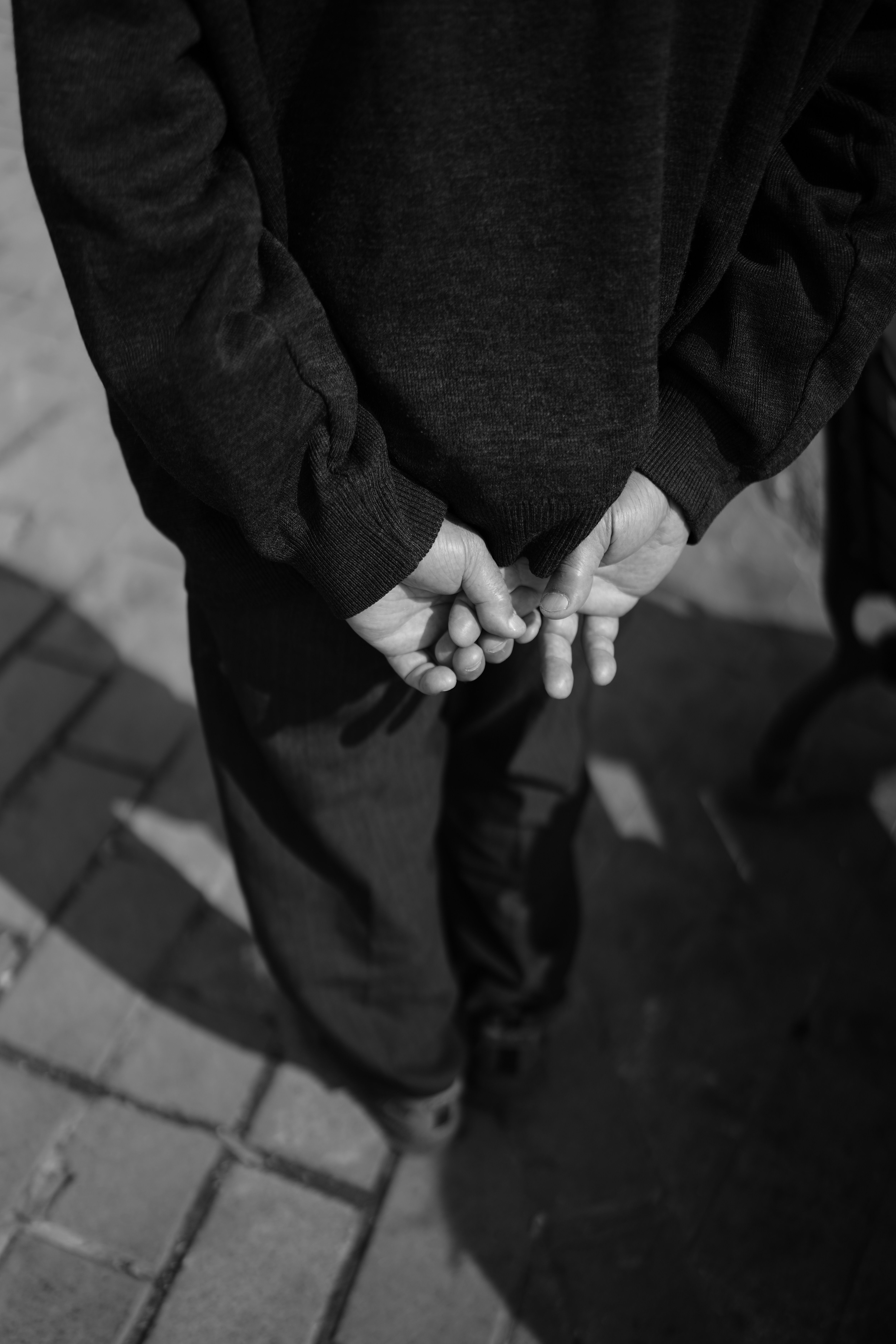 Monochrome photo of a child in a black outfit standing on pavement with hands held behind their back.