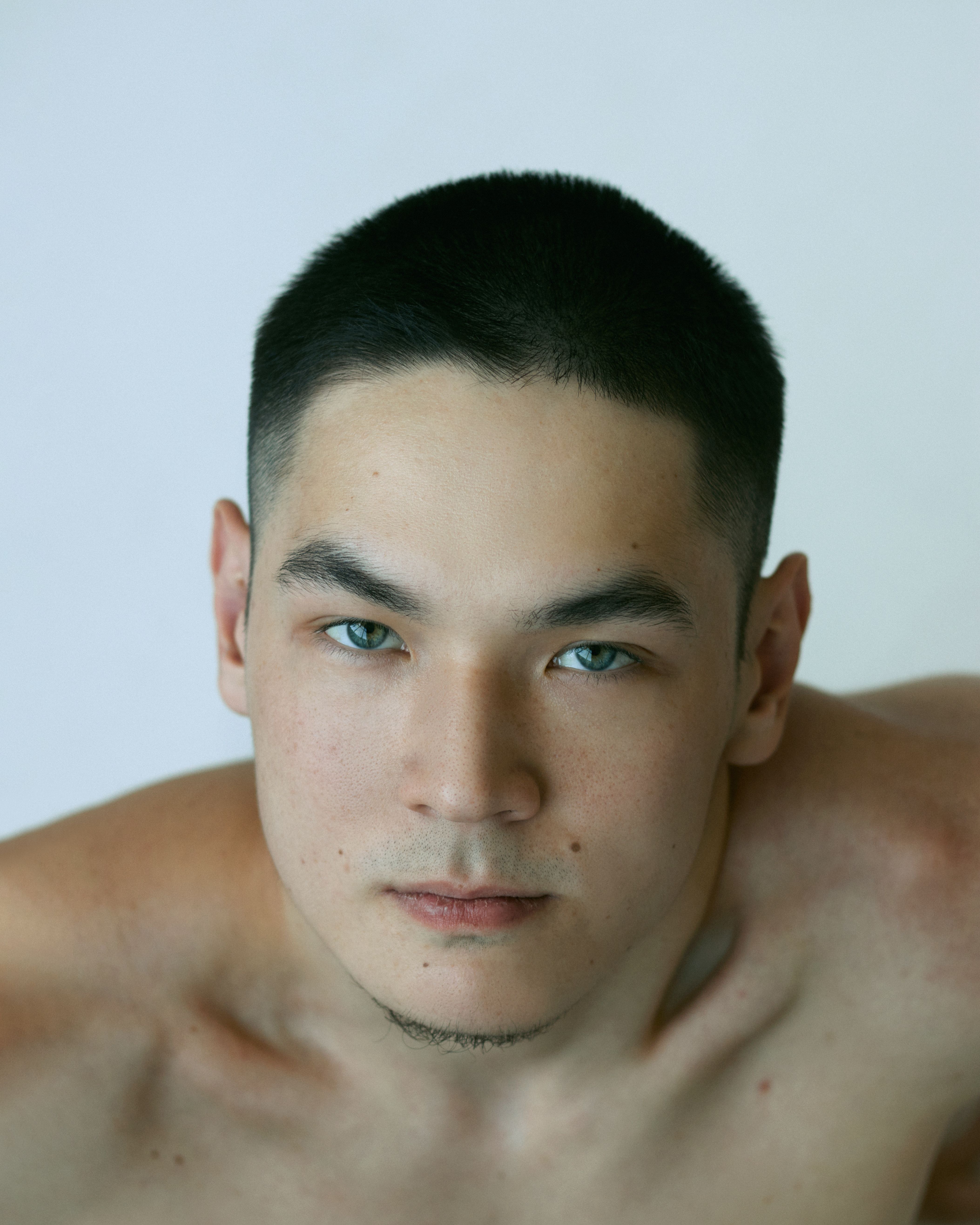Close-up portrait of a young, shirtless man with short hair against a plain background.