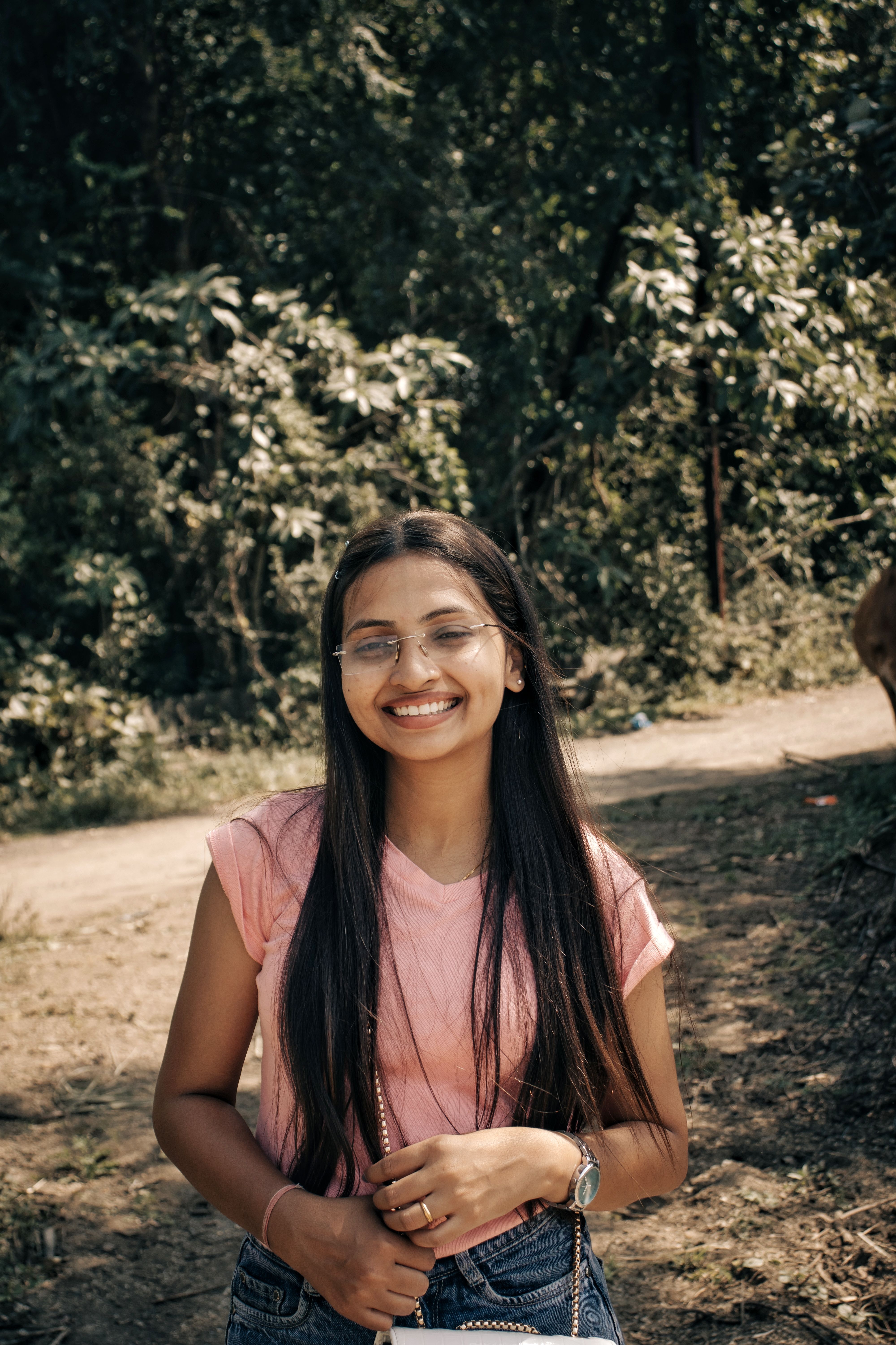 Happy young woman smiling under sunlight in a lush green park, conveying joy and relaxation.