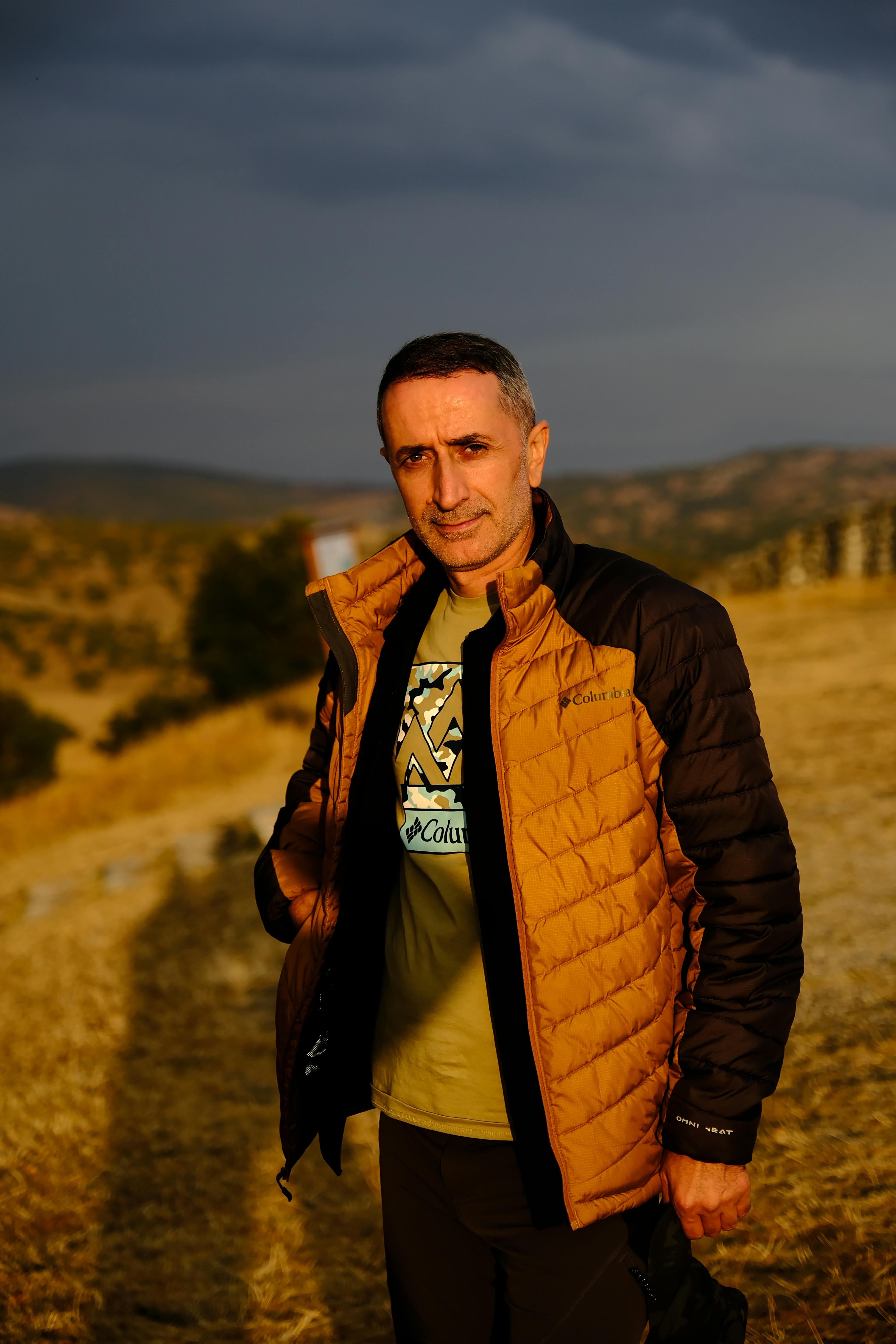 A man standing outdoors in an autumn landscape wearing a warm jacket.