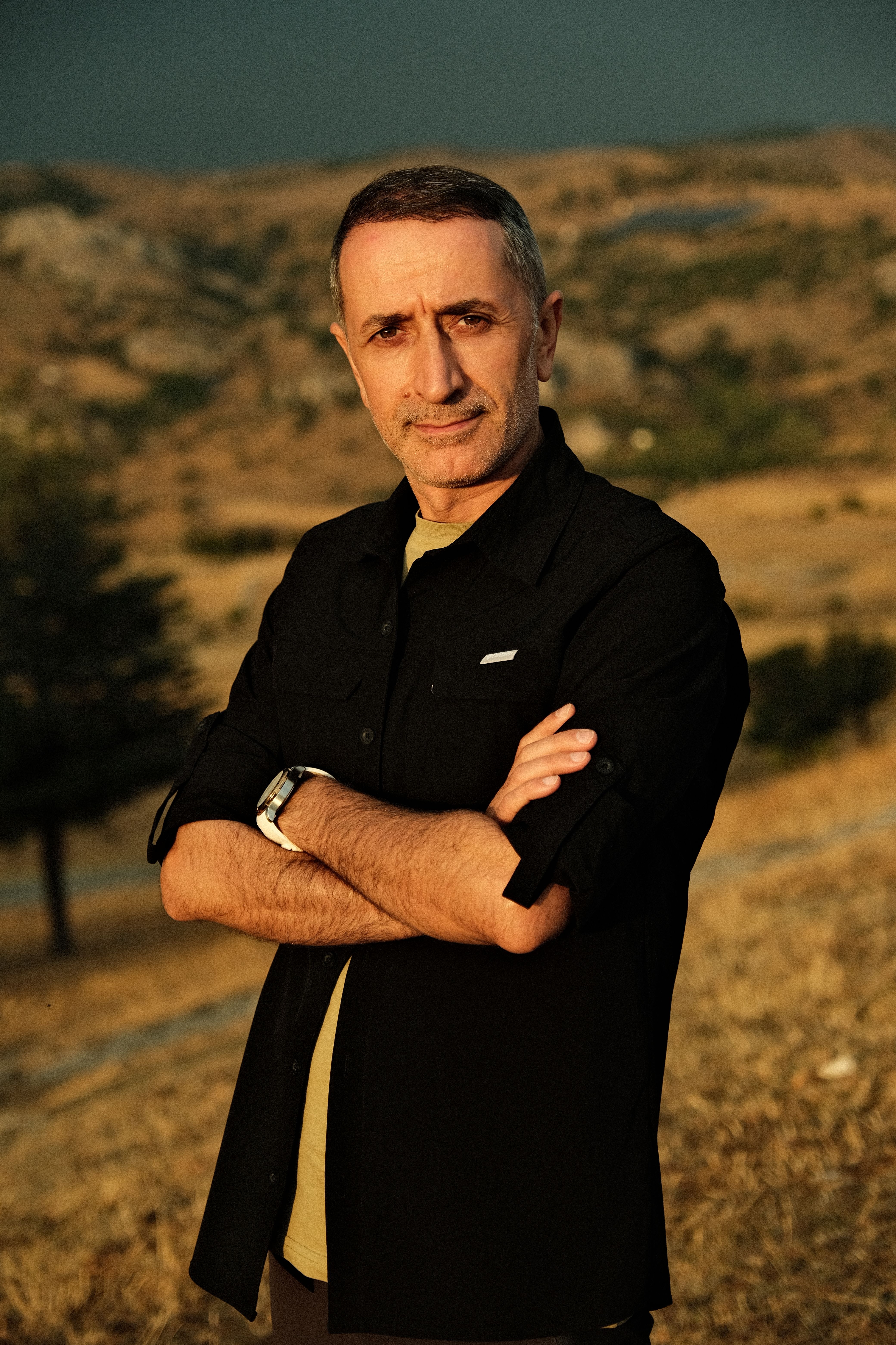 A confident man poses in a vast countryside landscape during golden hour.