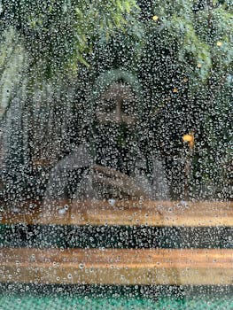 A mysterious reflection of a woman seen through a rain-soaked window, creating a dreamy and moody image.
