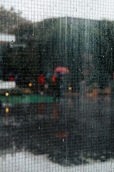 Raindrops trickle down a window, creating a blurred view of people with umbrellas outside.