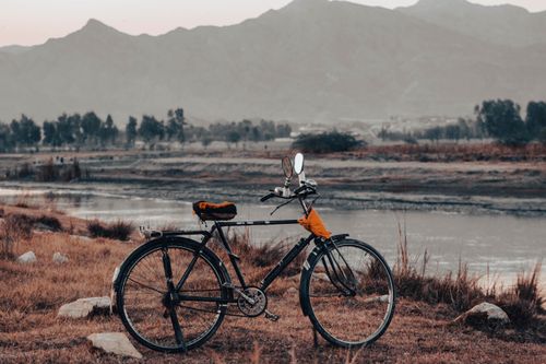 Free A tranquil view of a vintage bicycle by a serene mountain range and river at twilight. Stock Photo