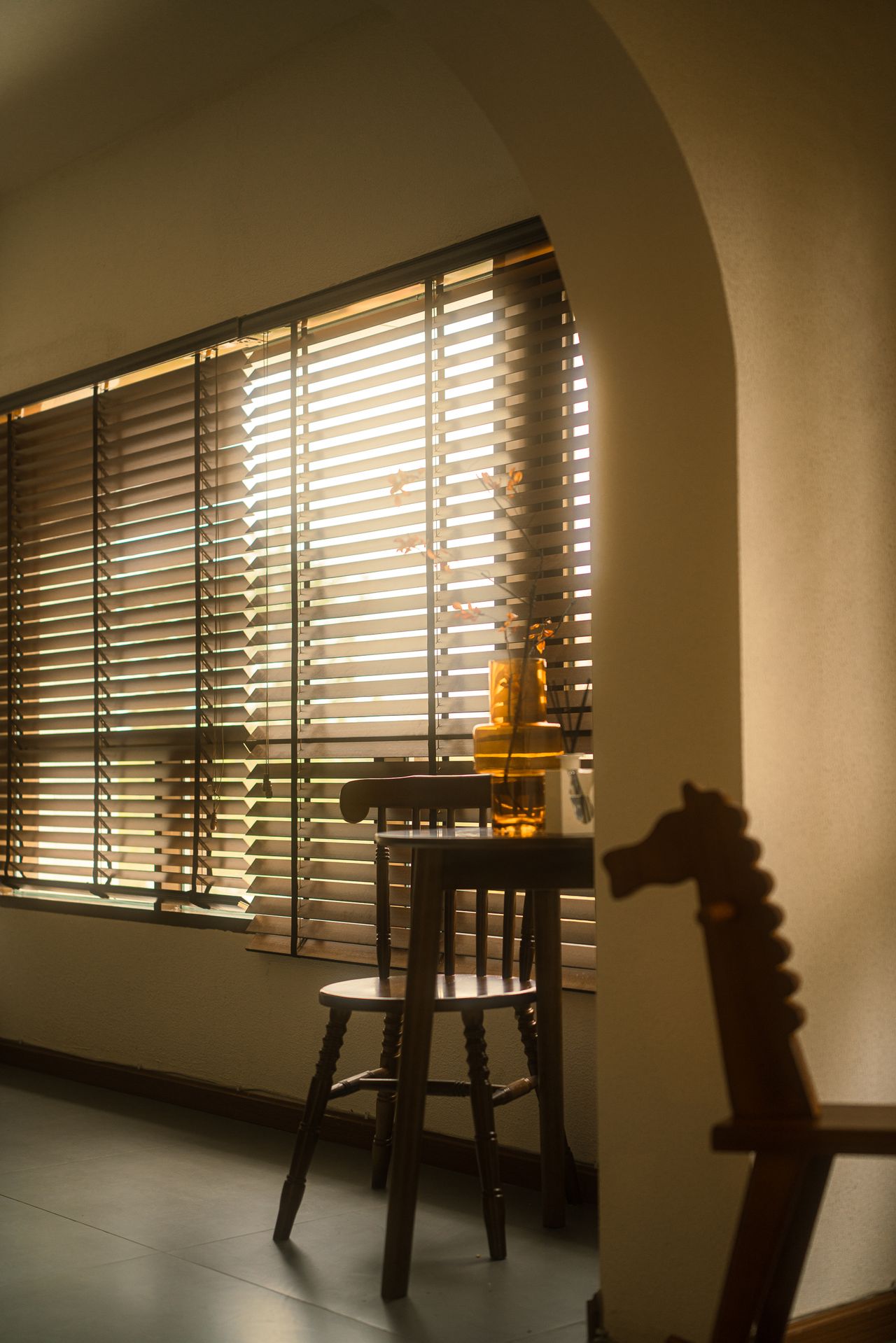 Wooden venetian blinds filtering golden sunlight over a small table and chair in a warm corner