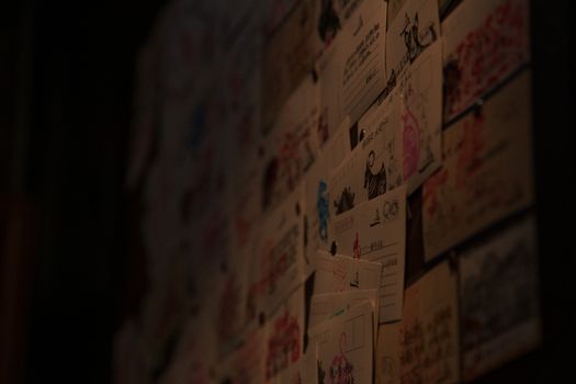 A creative display of diverse postcards and illustrations adorns a dimly lit wall.
