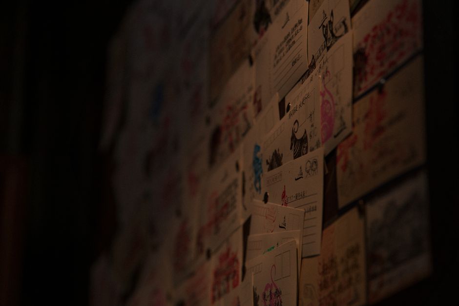 A creative display of diverse postcards and illustrations adorns a dimly lit wall.