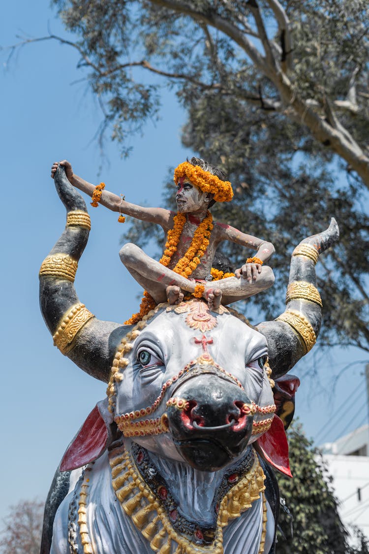 Man Wearing A Yellow Garland Sitting On A Bull Statue