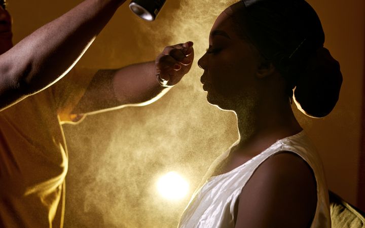 Hair stylist applying a spray mist on a client's hair in a dimly lit salon setting.