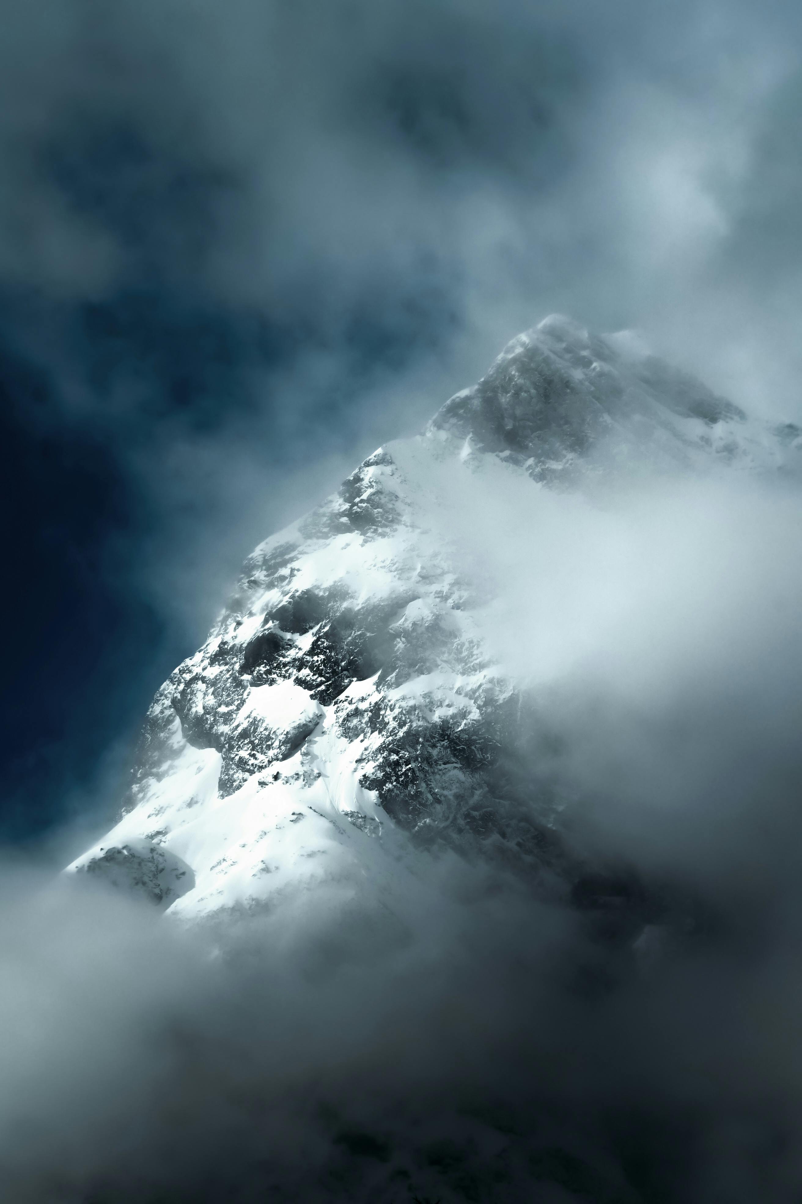 A breathtaking view of a snow-covered mountain peak surrounded by clouds and mist.