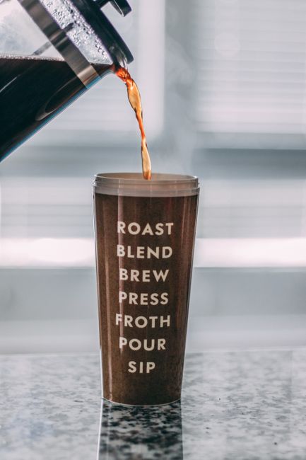 Coffee being poured into a tumbler with inspirational coffee-related text written vertically.