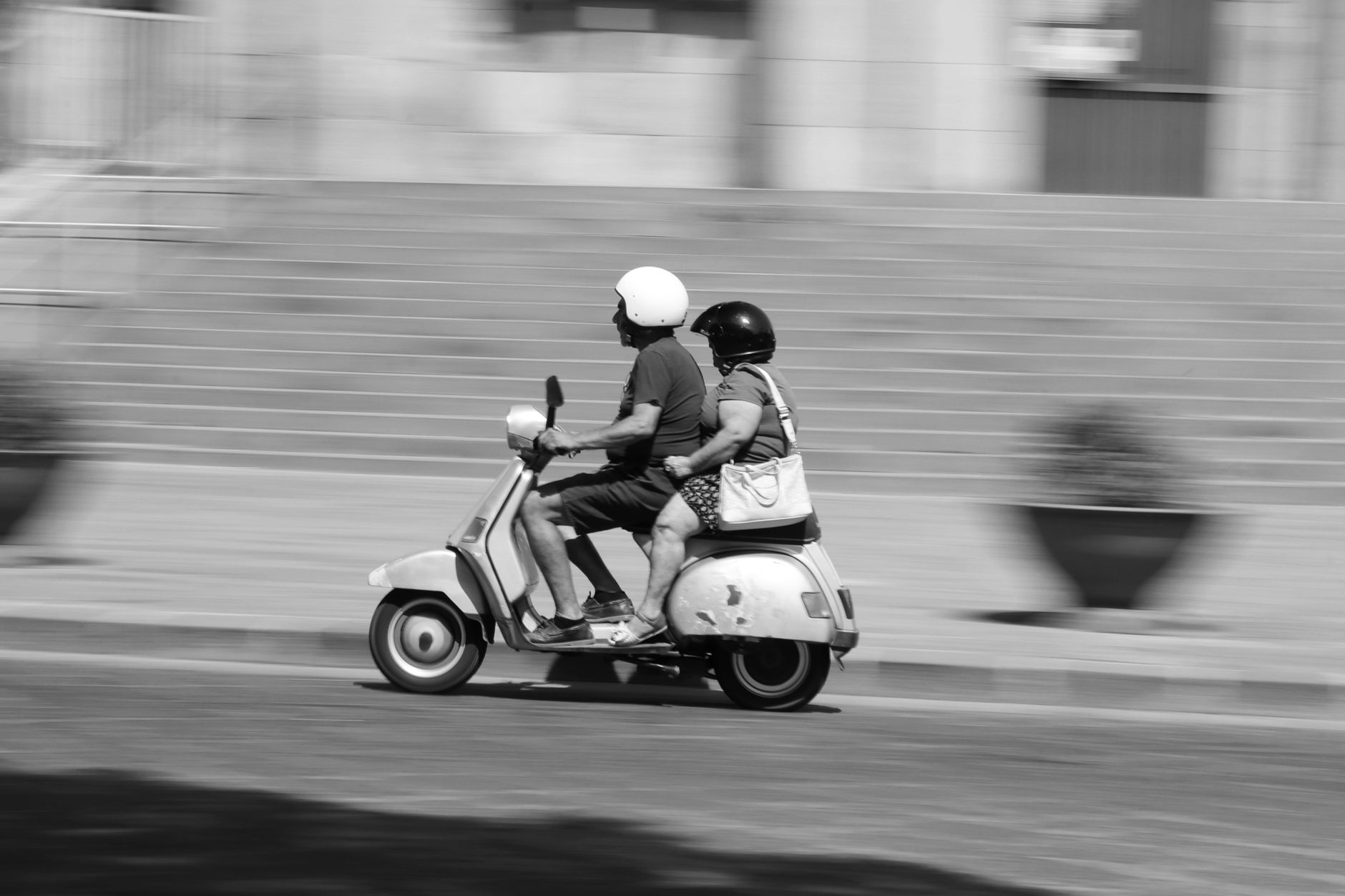 Two adults ride a Vespa through a Syracuse street.
