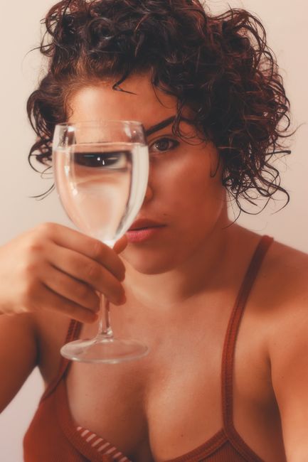 Artistic portrait of a woman holding a glass of water, focusing on the reflection and light play.