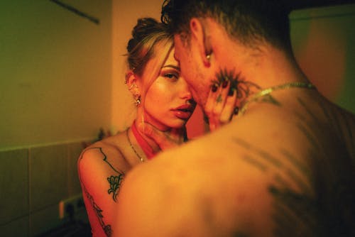 A close, intimate moment between a tattooed couple, captured in warm lighting.