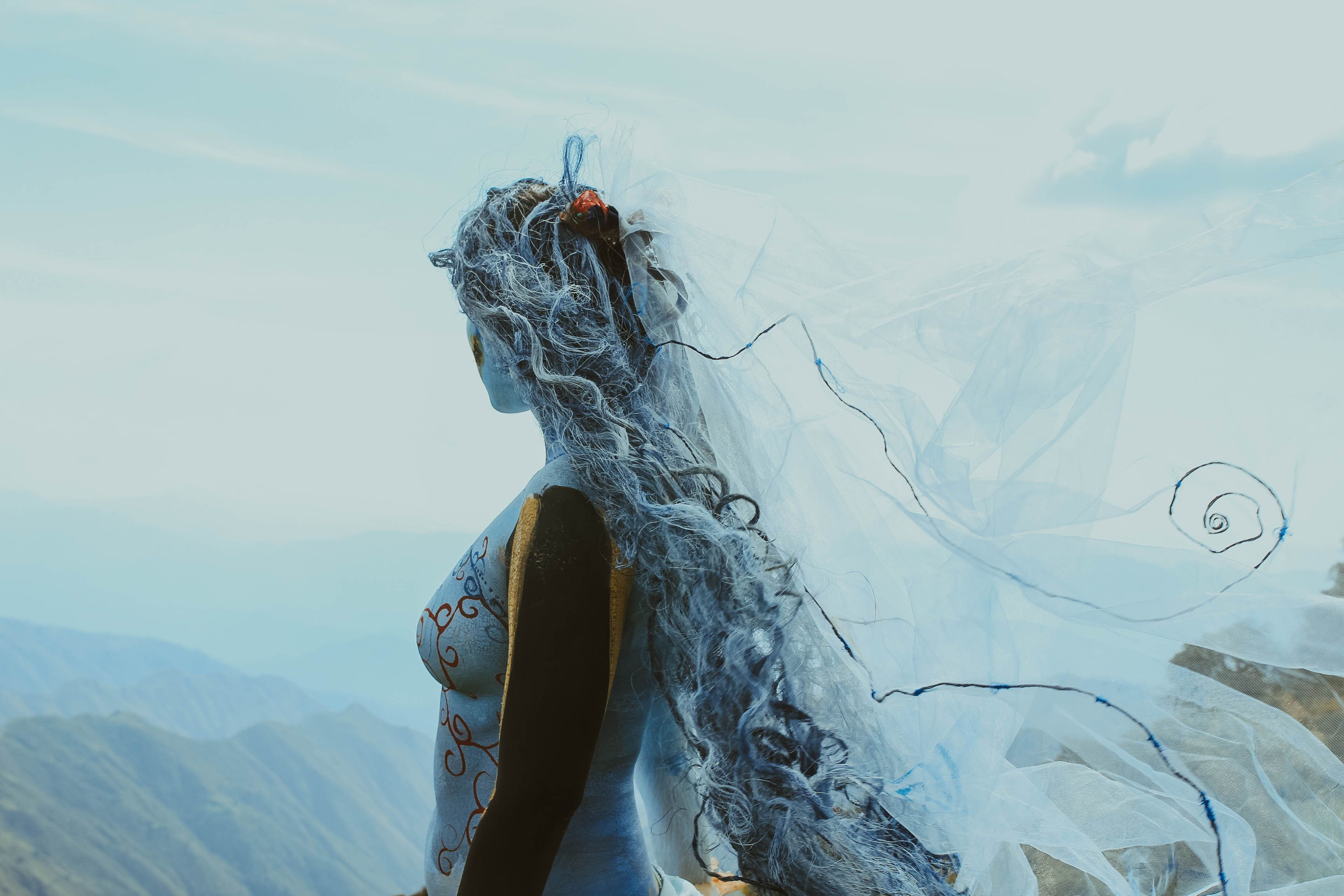 A person in cosplay with a painted body and flowing veil stands outdoors, embracing an artistic vision.