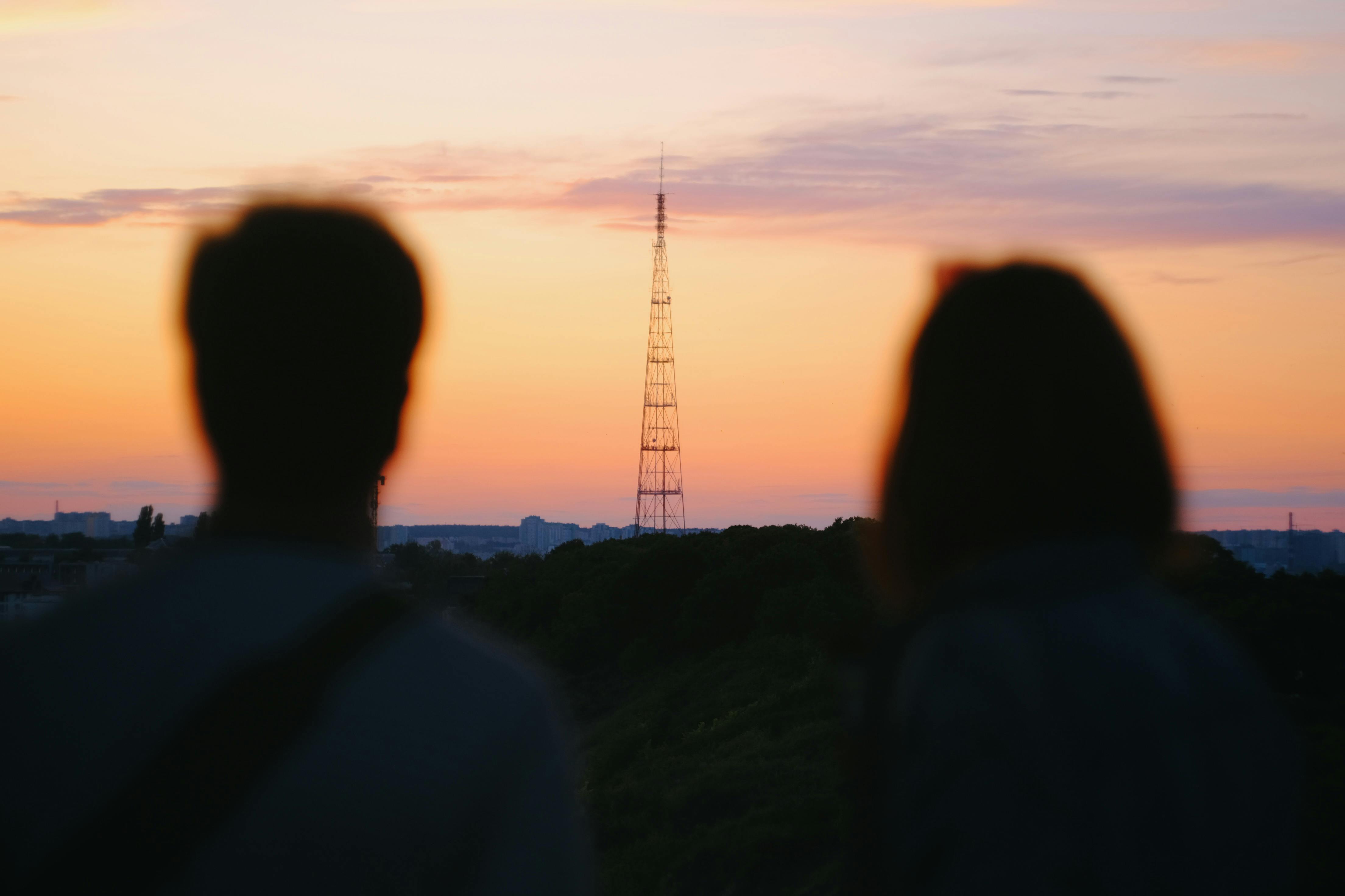Silhouette of a couple watching sunset over Kyiv skyline with radio tower.