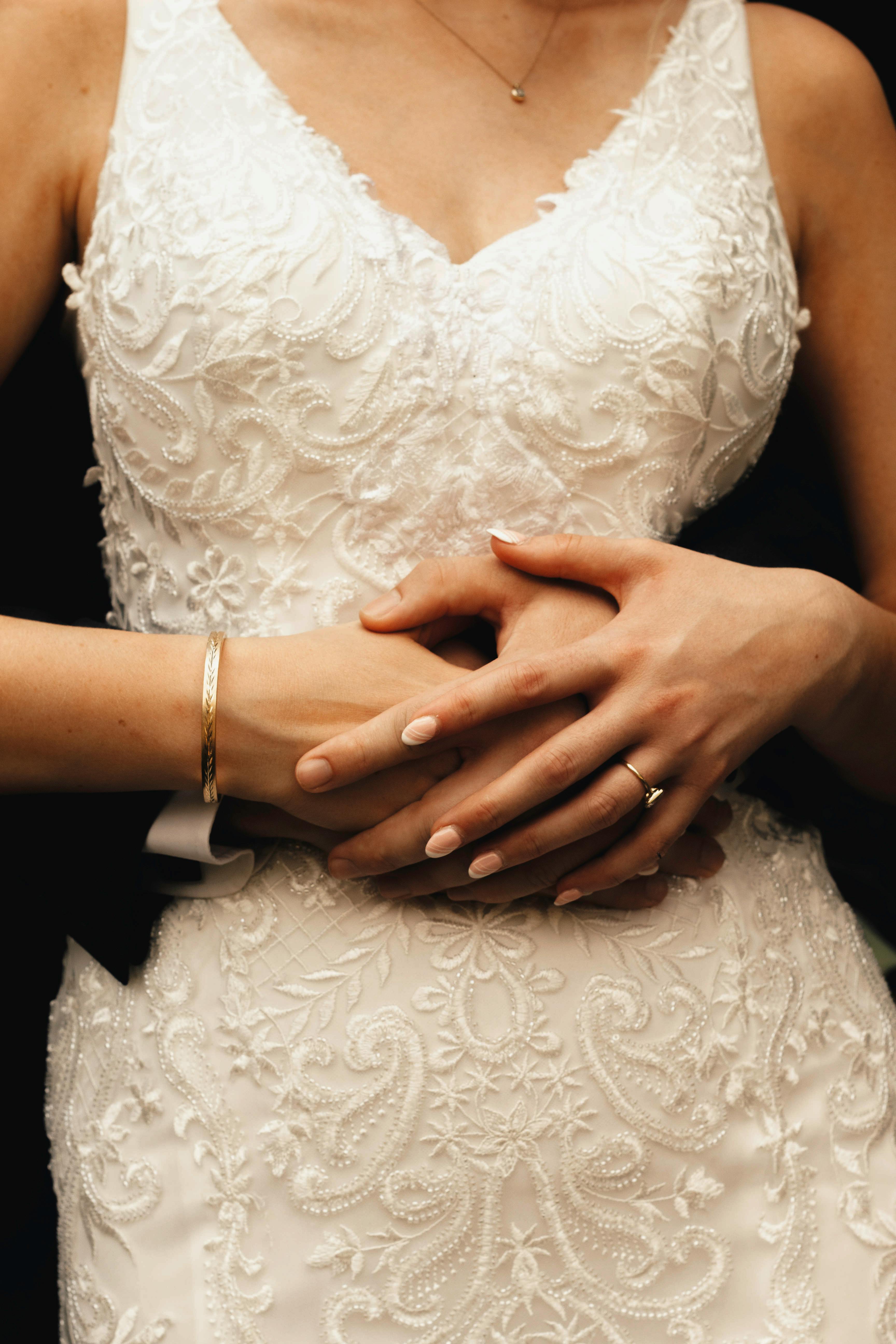 Close-up of a woman in an embroidered wedding dress with hands holding gently.