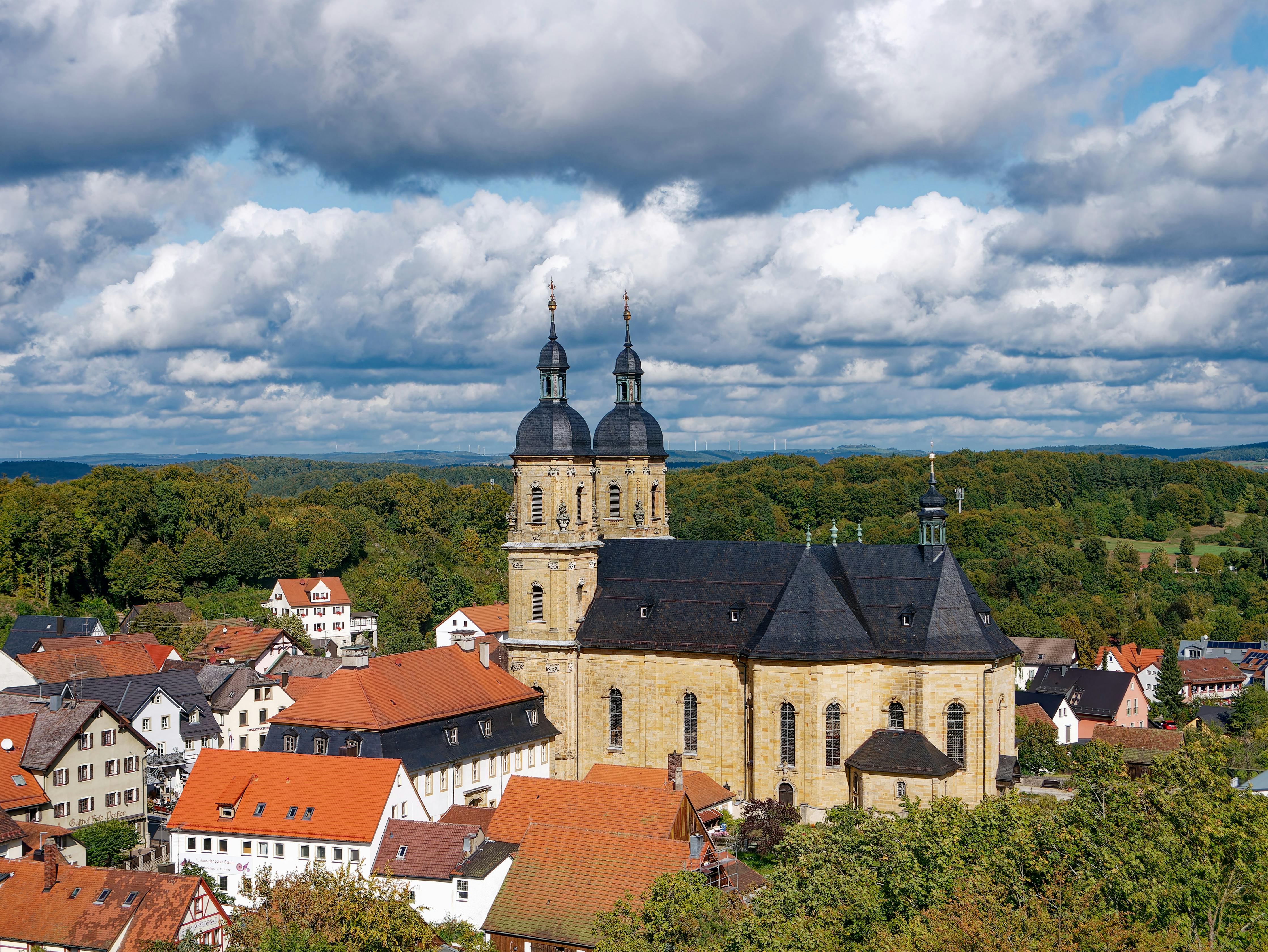 Aerial view of the Gößweinstein Basilica and quaint town in Bavaria under dramatic clouds.