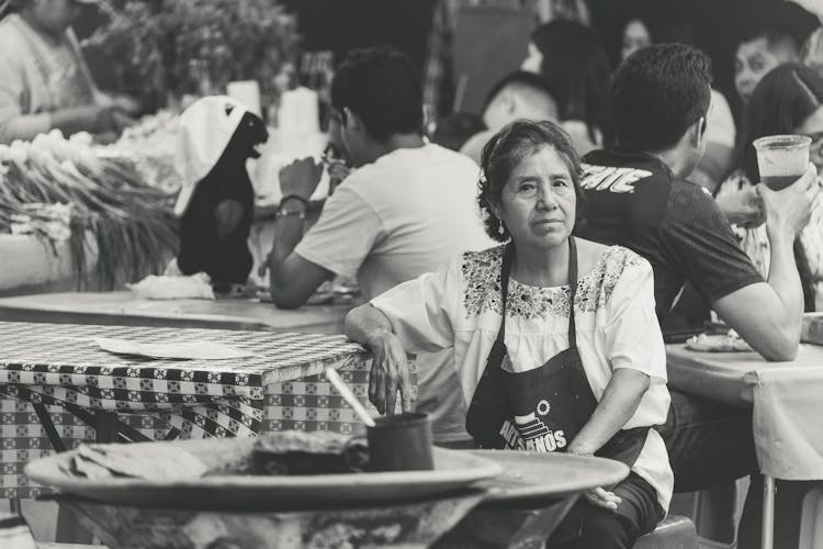 Woman In Apron Sitting Among People At Restaurant