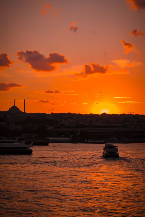 Free Scenic view of Istanbul mosque silhouette against a vibrant orange sunset with boats on the Bosphorus. Stock Photo