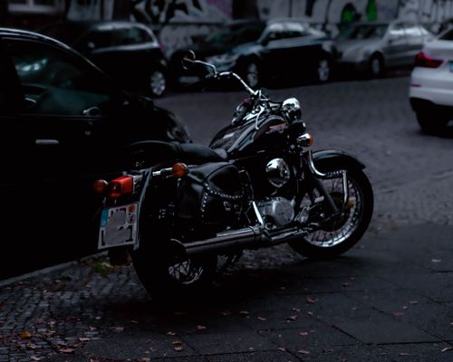 Free A sleek motorcycle parked on a city street, surrounded by cars, creating a moody urban scene. Stock Photo