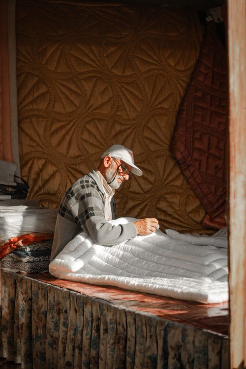 Free An elderly man intensely working on sewing quilts with natural lighting indoors. Stock Photo
