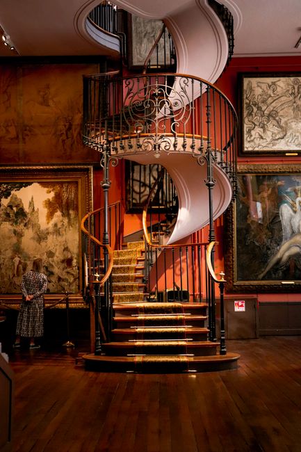 A stunning spiral staircase inside a Parisian art museum adorned with classic paintings.