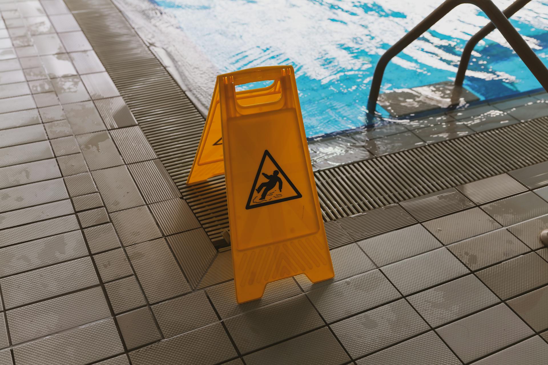 A caution wet floor sign placed near a swimming pool to ensure safety around the slippery area.