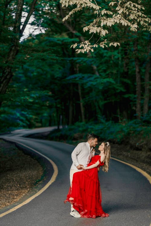 Man in Suit and Woman in Red Dress Posing Together on Road in Forest