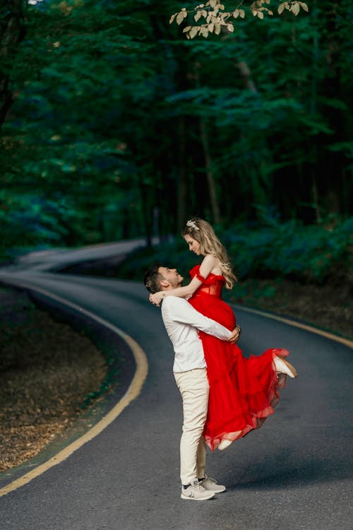 Man Hugging Woman in Red Dress on Road
