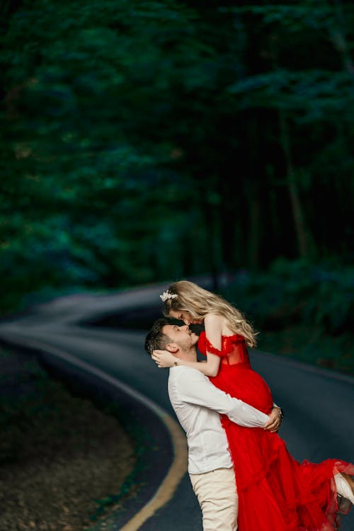 Man Hugging Woman in Red Dress on Road in Forest