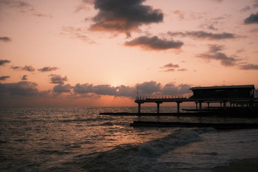 A tranquil seascape featuring a silhouetted pier at sunset over calm ocean waters.