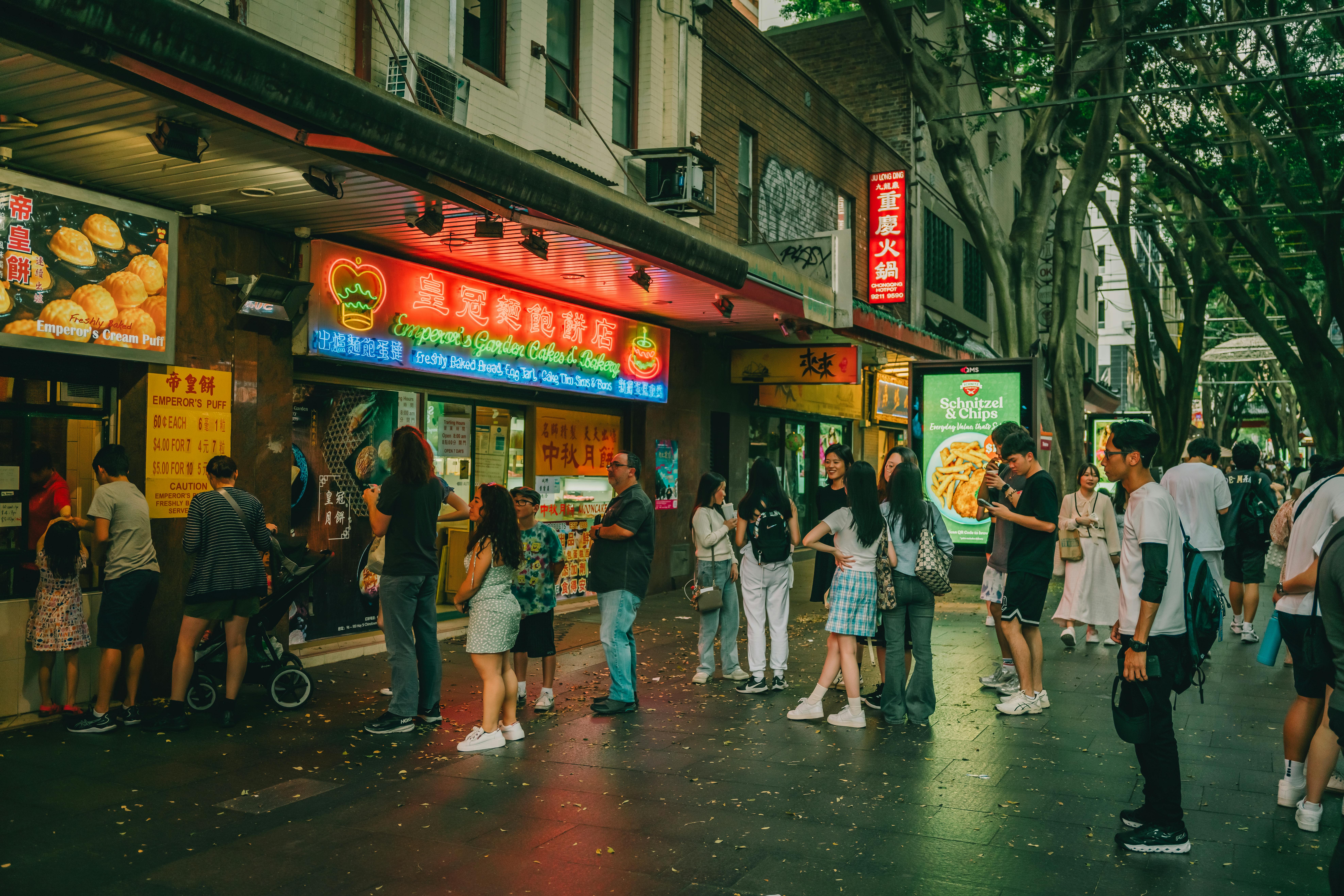 Street view of people enjoying Chinatown's eateries in Sydney during dusk with vivid neon lights.