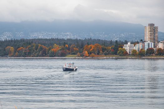 Scenic autumn view of Vancouver waterfront with a boat, colorful foliage, and city skyline.
