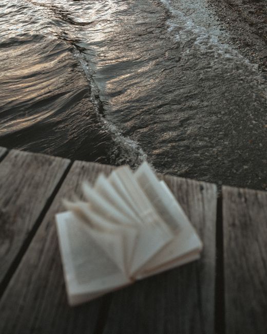 A serene scene of an open book on a wooden pier by a lake in Queenstown, New Zealand.
